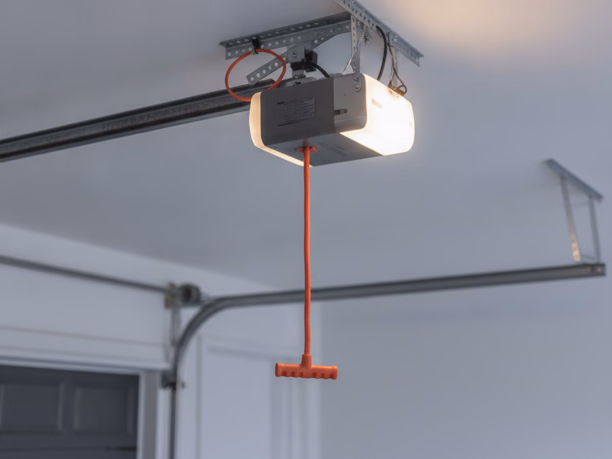 Red emergency release cord and handle hanging from a garage door opener rail